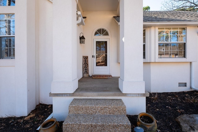 view of exterior entry with roof with shingles and stucco siding