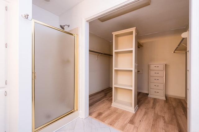 bathroom featuring wood finished floors, a stall shower, and a spacious closet