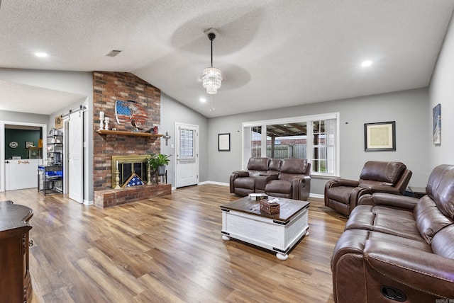 living area featuring wood finished floors, visible vents, vaulted ceiling, a textured ceiling, and a barn door