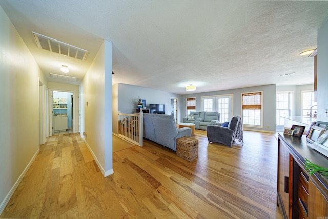 unfurnished living room featuring baseboards, visible vents, light wood finished floors, and a textured ceiling