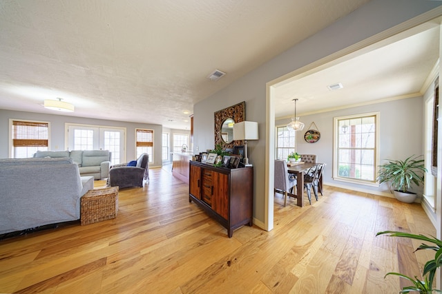 living area featuring visible vents, crown molding, light wood-type flooring, and baseboards