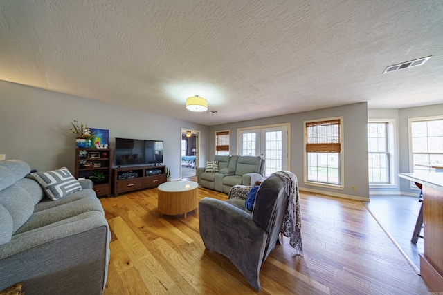 living room with a wealth of natural light, visible vents, light wood finished floors, and a textured ceiling