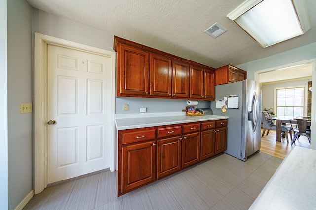 kitchen with visible vents, a textured ceiling, light countertops, and stainless steel refrigerator with ice dispenser