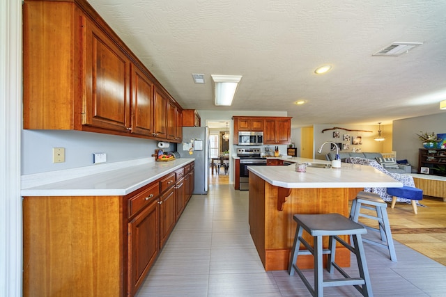 kitchen with visible vents, a kitchen bar, light countertops, stainless steel appliances, and a sink