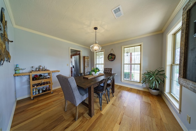 dining space featuring light wood finished floors, visible vents, crown molding, baseboards, and a chandelier