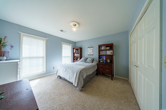 bedroom featuring light carpet, visible vents, baseboards, and a closet