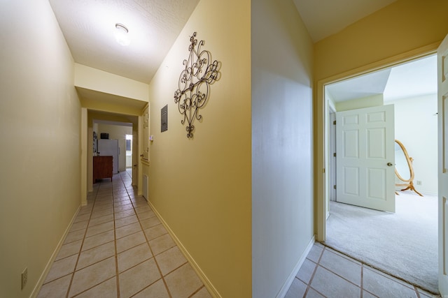 hall featuring light tile patterned floors, baseboards, and light colored carpet