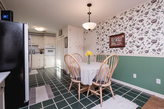 dining space with a wainscoted wall, baseboards, dark tile patterned flooring, and wallpapered walls