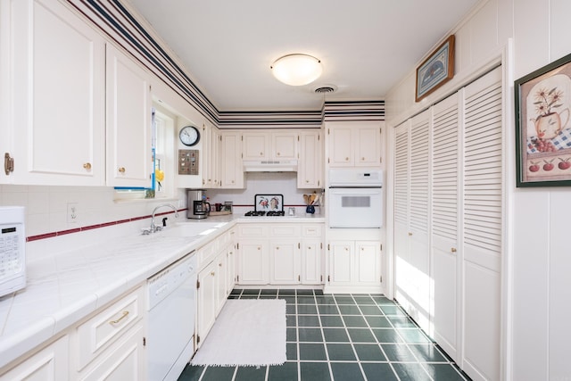 kitchen with visible vents, tile counters, under cabinet range hood, white appliances, and white cabinetry