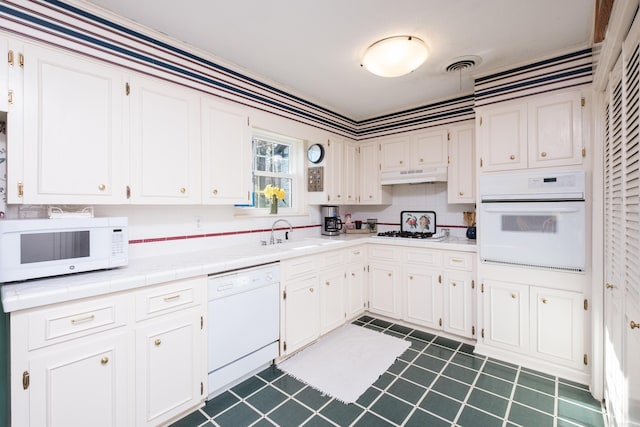 kitchen with visible vents, under cabinet range hood, a sink, white cabinetry, and white appliances