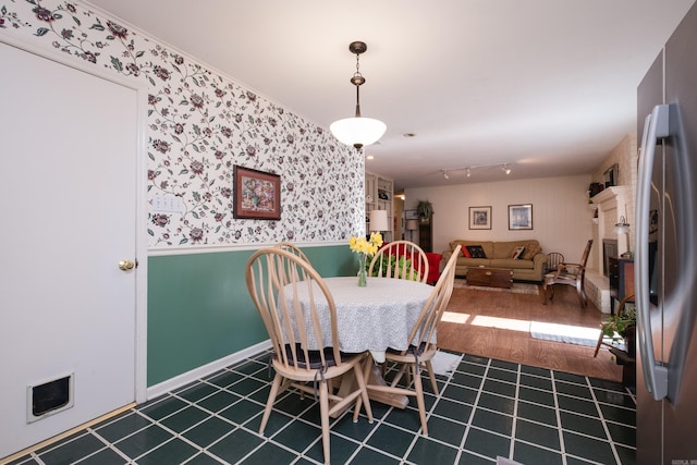 dining area featuring wallpapered walls, a wainscoted wall, wood finished floors, and baseboards