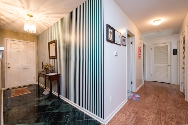 hall featuring wood finished floors, baseboards, and a chandelier