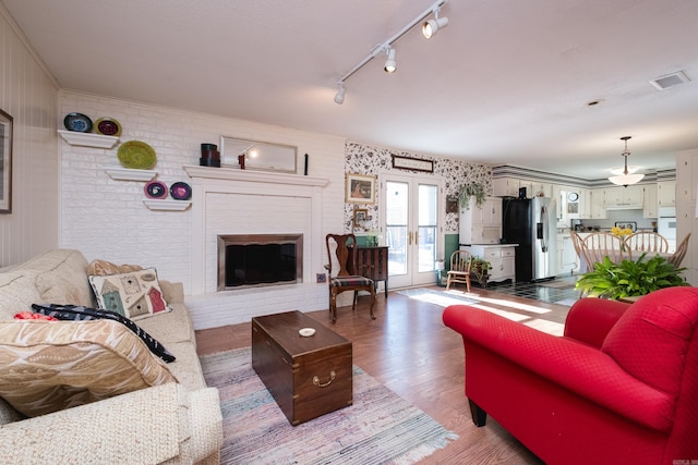 living area featuring wood finished floors, visible vents, ornamental molding, french doors, and a brick fireplace