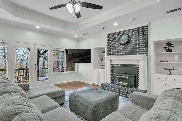 living room with visible vents, built in features, wood finished floors, crown molding, and a raised ceiling