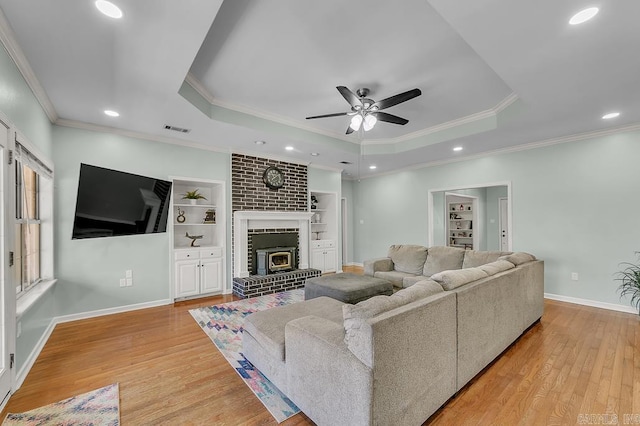 living area with light wood-type flooring, visible vents, built in features, a tray ceiling, and baseboards