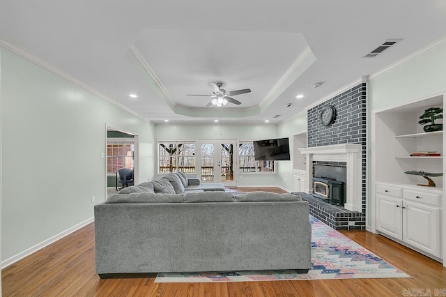 living room with a tray ceiling, visible vents, wood finished floors, and ornamental molding