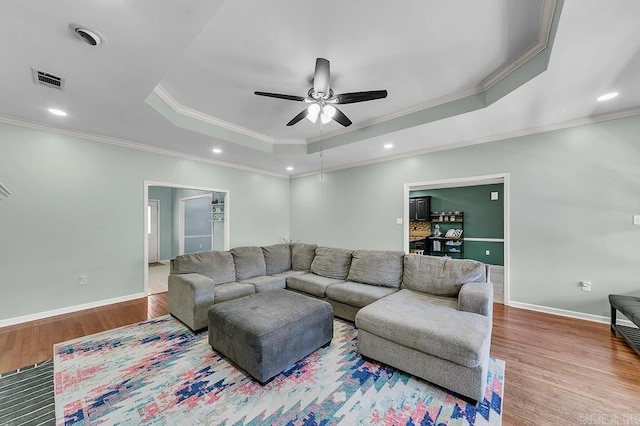 living room featuring baseboards, a ceiling fan, a tray ceiling, and wood finished floors