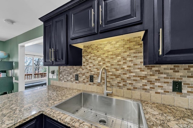 kitchen featuring dark cabinetry, light stone countertops, backsplash, and a sink