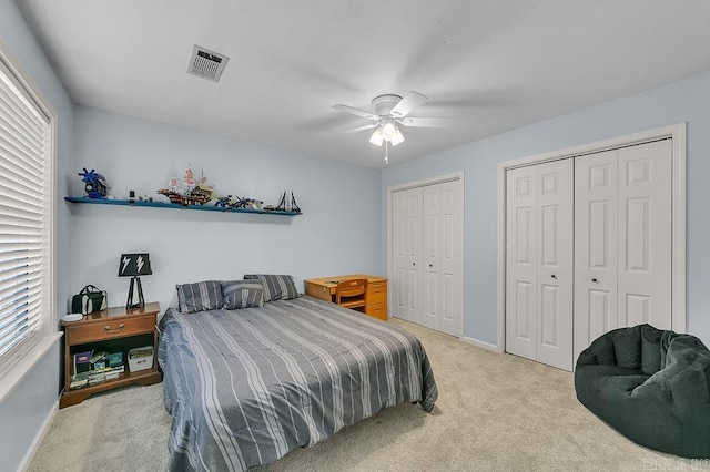 bedroom with visible vents, baseboards, multiple closets, ceiling fan, and light colored carpet