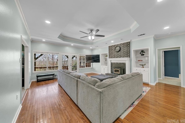 living area featuring a tray ceiling, light wood-type flooring, visible vents, and crown molding