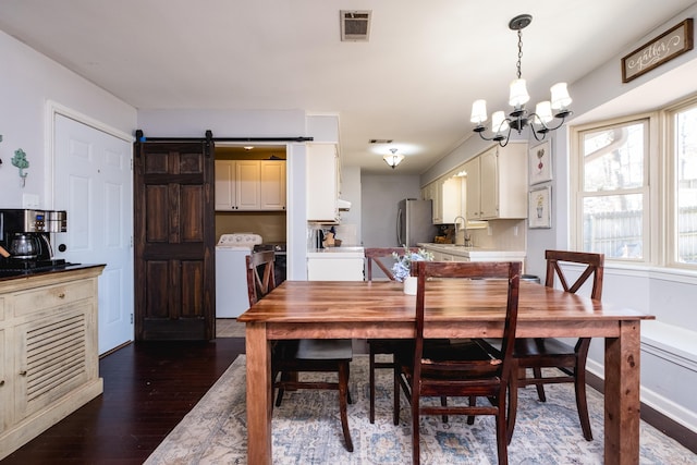 dining room with visible vents, an inviting chandelier, dark wood-type flooring, a barn door, and independent washer and dryer