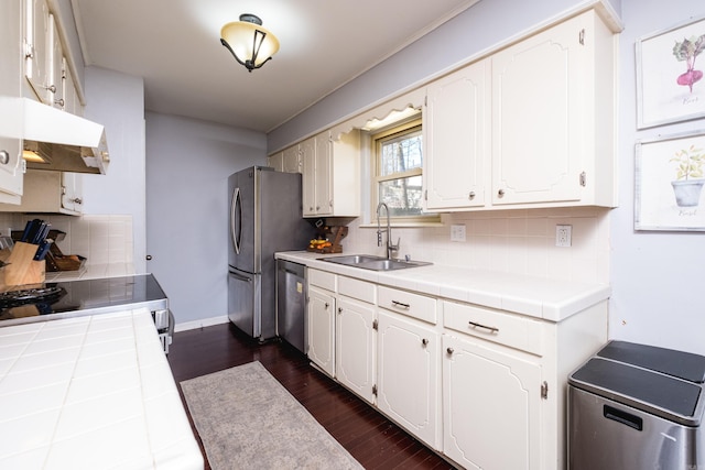 kitchen featuring backsplash, tile countertops, appliances with stainless steel finishes, white cabinets, and a sink