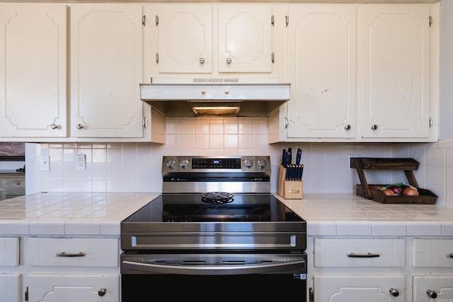 kitchen featuring stainless steel electric stove, decorative backsplash, tile counters, white cabinets, and under cabinet range hood