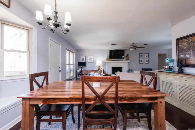 dining room featuring a brick fireplace, dark wood-style flooring, and ceiling fan with notable chandelier