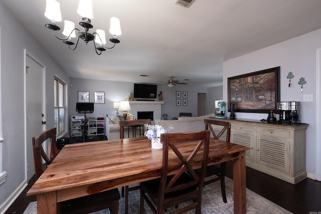 dining space with baseboards, dark wood-style flooring, a fireplace, and ceiling fan with notable chandelier