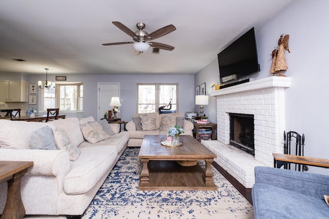 living room with a wealth of natural light, visible vents, ceiling fan with notable chandelier, and a brick fireplace