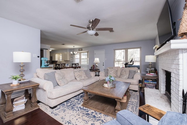 living area featuring wood finished floors, a fireplace, and ceiling fan with notable chandelier