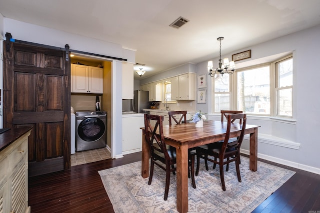 dining space with dark wood finished floors, a barn door, visible vents, and washing machine and clothes dryer