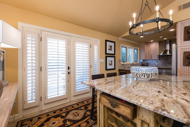 kitchen featuring tasteful backsplash, visible vents, light stone counters, and wall chimney range hood