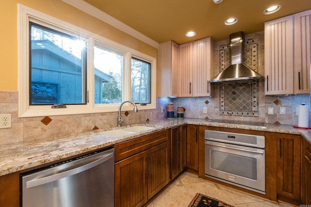 kitchen with a sink, backsplash, appliances with stainless steel finishes, wall chimney exhaust hood, and light stone countertops