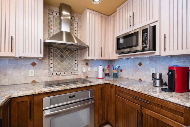 kitchen with wall chimney range hood, light stone counters, backsplash, and stainless steel appliances