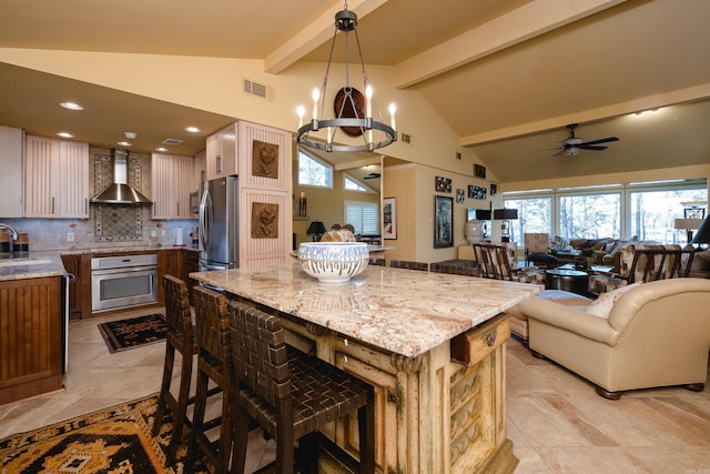 kitchen with a sink, wall chimney range hood, open floor plan, and stainless steel appliances