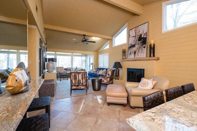 living room featuring beamed ceiling, high vaulted ceiling, wooden walls, a brick fireplace, and a healthy amount of sunlight