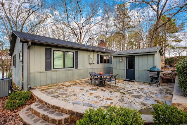 back of property with a patio, an outdoor structure, central AC, and a chimney