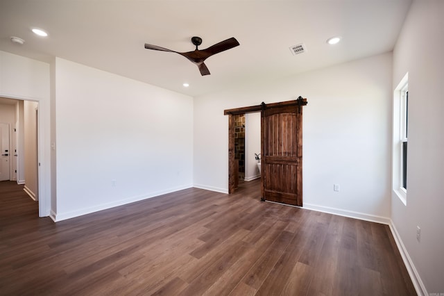 empty room with visible vents, ceiling fan, dark wood finished floors, a barn door, and recessed lighting