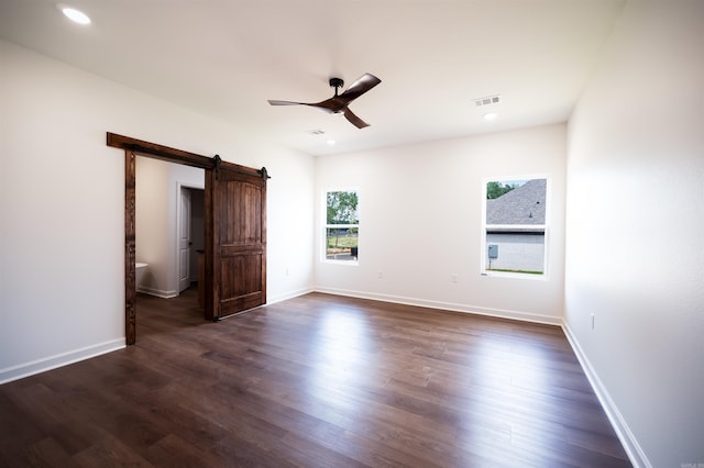 unfurnished bedroom with a barn door, baseboards, visible vents, and dark wood-style flooring