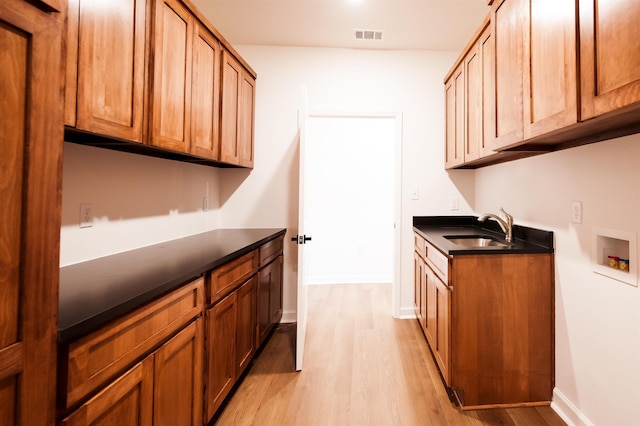 kitchen with a sink, light wood-type flooring, dark countertops, and brown cabinetry