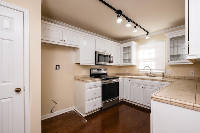 kitchen with appliances with stainless steel finishes, white cabinetry, glass insert cabinets, and a sink