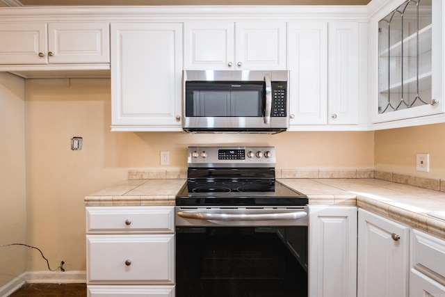 kitchen with glass insert cabinets, baseboards, appliances with stainless steel finishes, and white cabinets