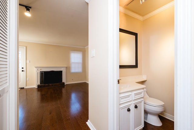 bathroom featuring a brick fireplace, crown molding, baseboards, toilet, and wood finished floors