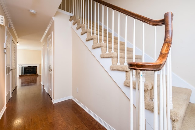 staircase with a fireplace with raised hearth, wood finished floors, baseboards, and ornamental molding