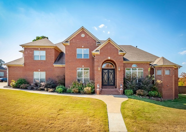 traditional-style home with brick siding, a front yard, and roof with shingles