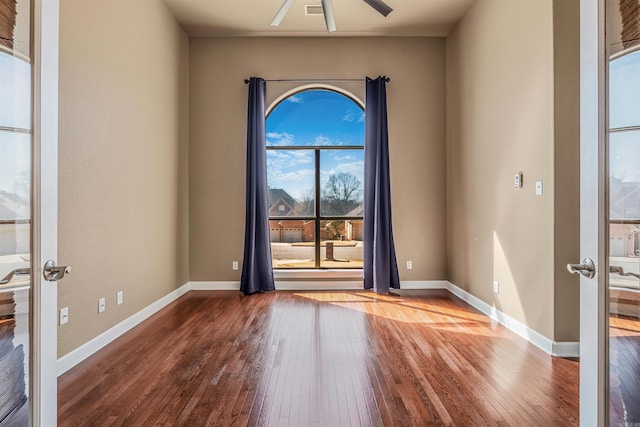 empty room featuring french doors, a ceiling fan, baseboards, and hardwood / wood-style flooring