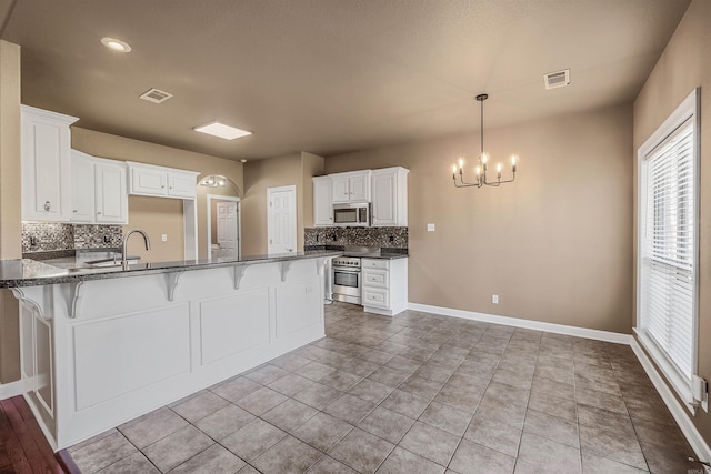 kitchen featuring visible vents, a kitchen bar, appliances with stainless steel finishes, and a peninsula