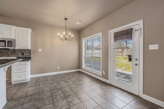 unfurnished dining area with tile patterned flooring, baseboards, visible vents, and a chandelier