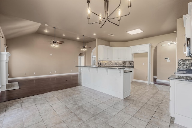 kitchen featuring ceiling fan, open floor plan, light tile patterned floors, a peninsula, and arched walkways